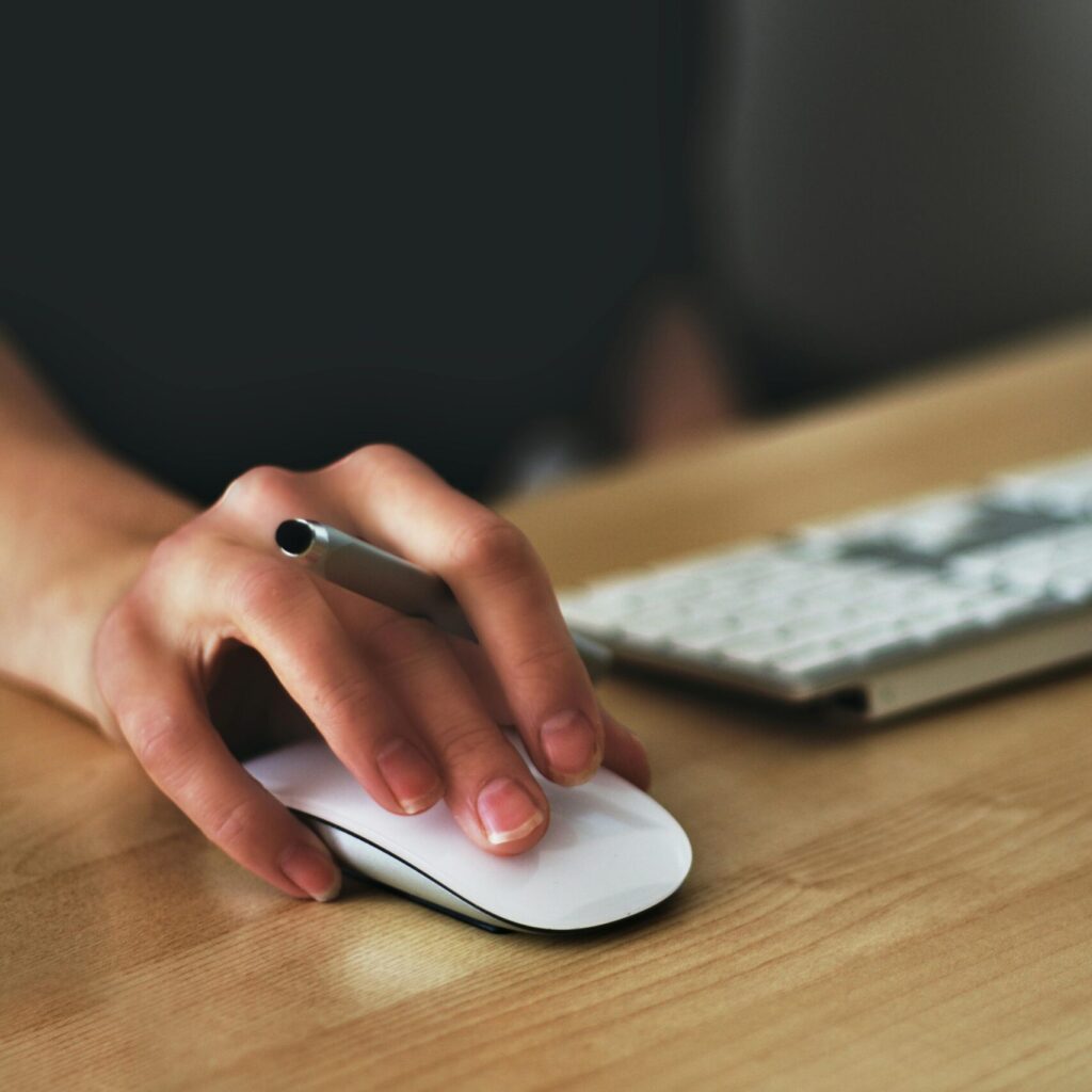 A hand using a wireless mouse at a modern desk setup with a computer and keyboard.